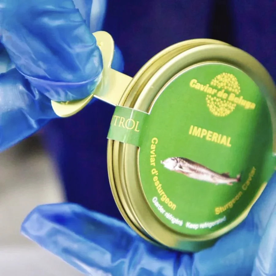 A gloved hand opening the tamper seal on a Caviar de Beluga Imperial tin